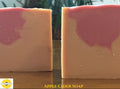 Two rectangular bars of apple cider soap standing upright on a wooden surface, with a pink swirl pattern on a warm peach-beige base. The left bar is partially cropped. The words "Apple Cider Soap" and the Sunlit Soaps logo is on the bottom edge.