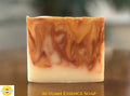 A rectangular bar of artisan soap with a marbled swirl pattern of orange, brown, and creamy white, resting on a reflective wooden surface. The text 'AUTUMN ESSENCE SOAP' is printed at the bottom, and a 'Sunlit Soaps' logo is in the bottom-left corner.