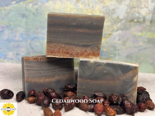 
Three stacked  Cedarwood soap bars with a natural, earthy color pattern, surrounded by dried fruits on a textured surface with Sunlit Soaps branding.