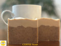Two rectangular bars of handmade coffee soap in a layered beige and brown speckled design, displayed on a wooden surface with a white ceramic mug in the blurred background. A 'Sunlit Soaps' logo is visible in the bottom-left corner, and 'COFFEE SOAP' is written in yellow text at the bottom.