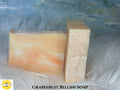 Two bars of Grapefruit Bellini soap on a textured white surface with a blurred blue background with Sunlit Soaps branding.