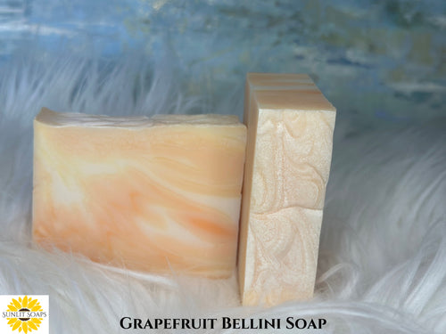 Two bars of Grapefruit Bellini soap on a textured white surface with a blurred blue background with Sunlit Soaps branding.