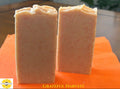 Two bars of orange flecked soap on a bright orange mat. The words "Grateful Harvest" is along the bottom and the Sunlit Soaps brand logo.