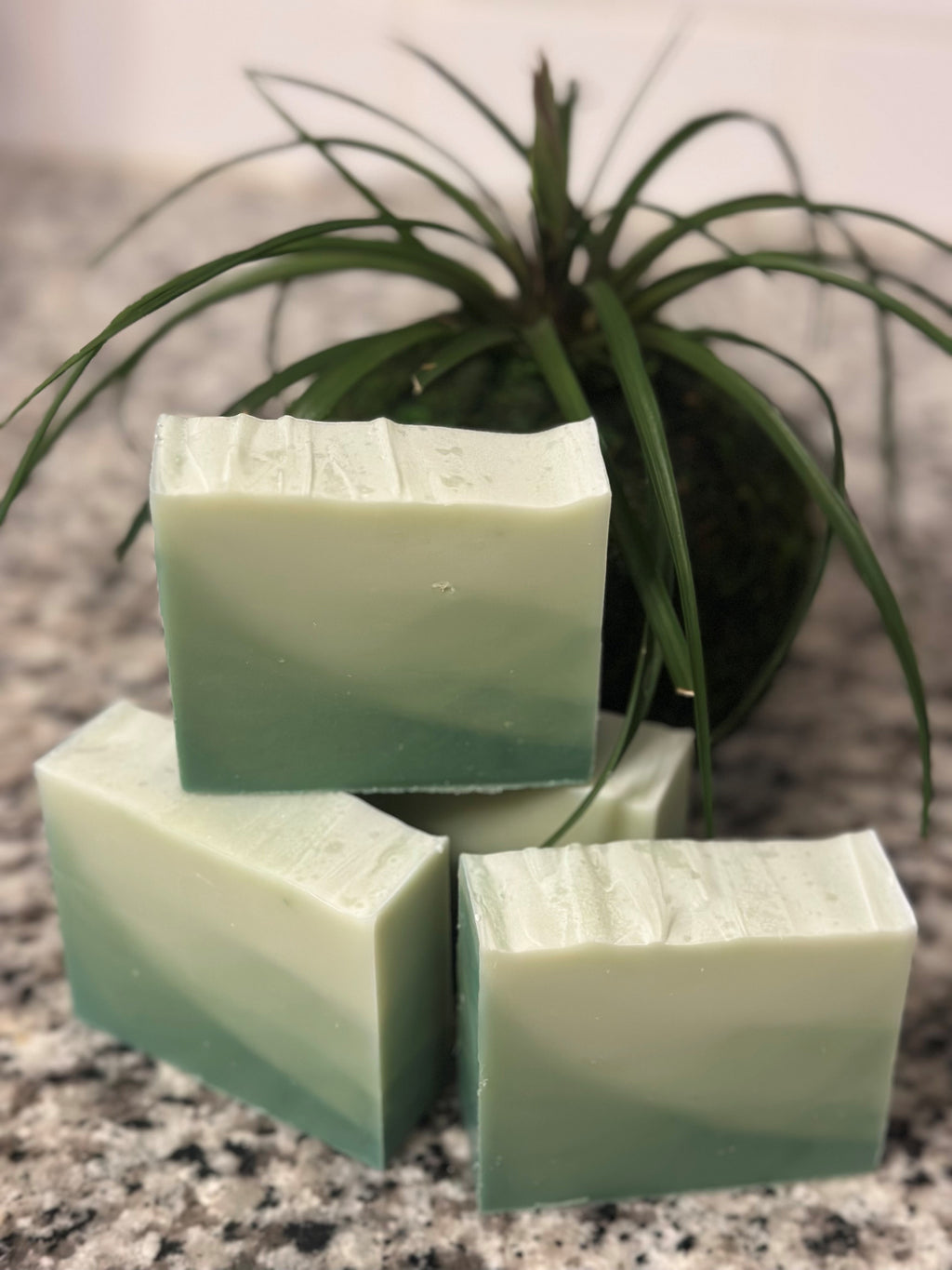 Three green ombre soap bars stacked on a speckled surface with a plant in the background. Branded title Sunlit Soaps.