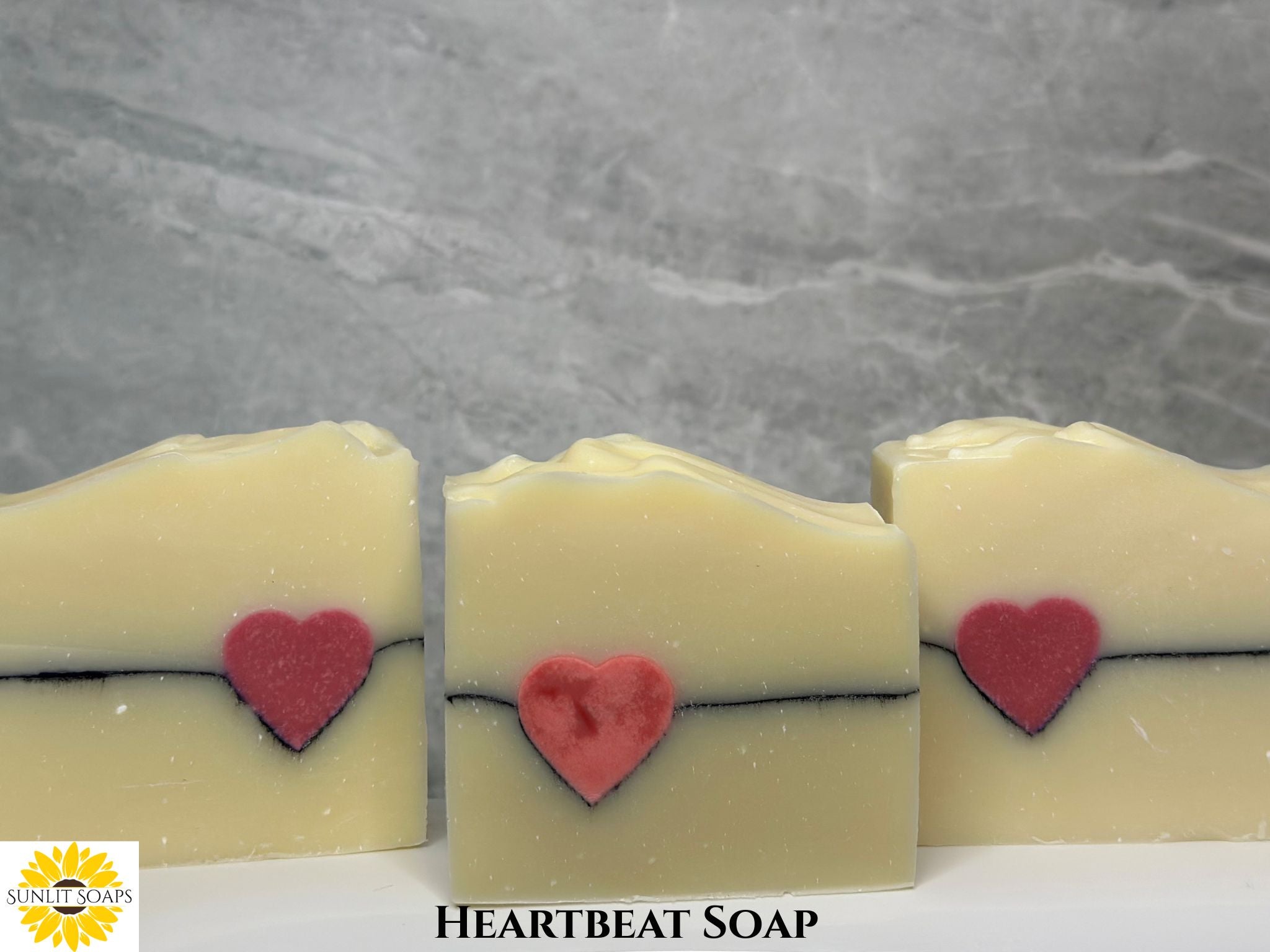 Heartbeat soap bars with red hearts on a gray background with text and Sunlit Soaps Logo